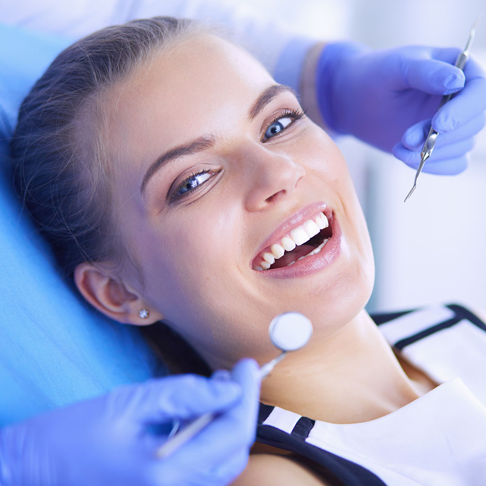 A woman sitting on a dental chair with a smile, receiving dental care from a professional.
