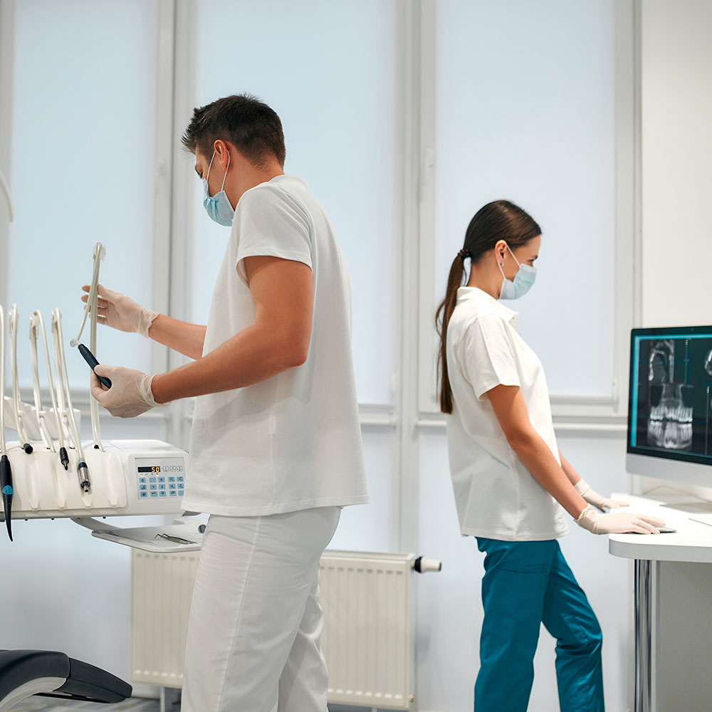 The image shows two individuals wearing white coats standing behind a medical workstation with various pieces of equipment, including what appears to be an MRI machine.